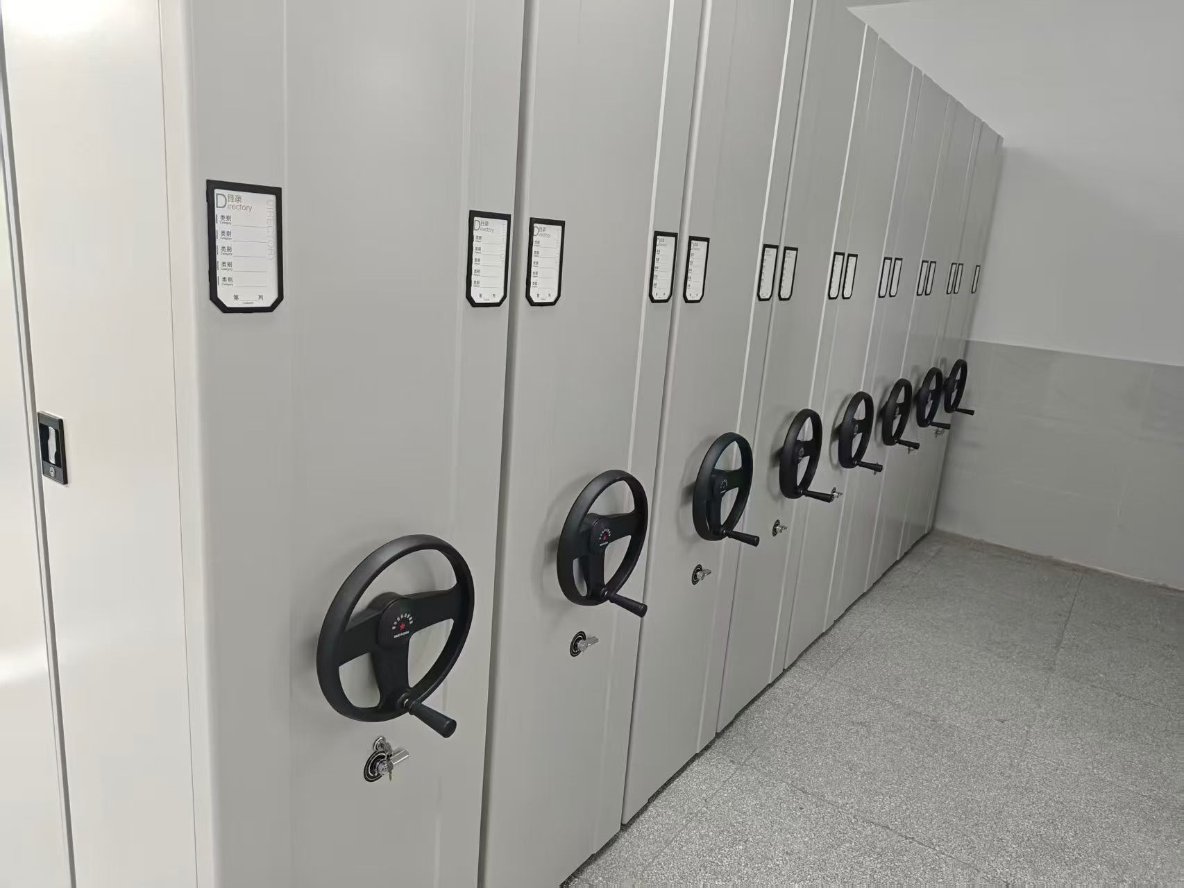 Installed white high-density mobile shelving system with black hand wheels and individual locks